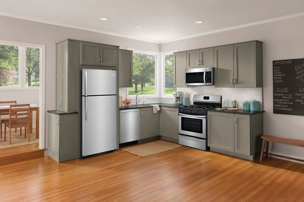 Stainless steel top freezer refrigerator in a modern kitchen with sage green cabinets and white walls 