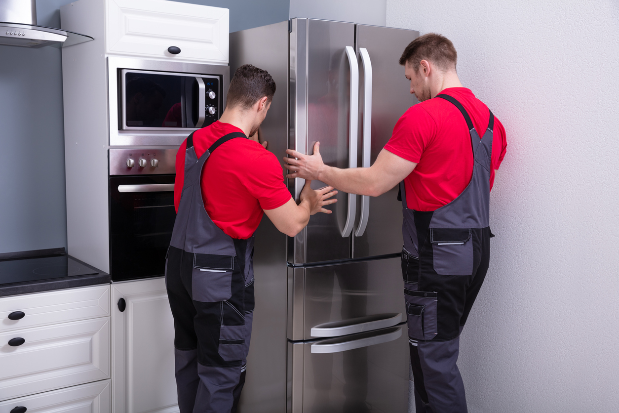 two deliverymen move new stainless-steel French door refrigerator into place