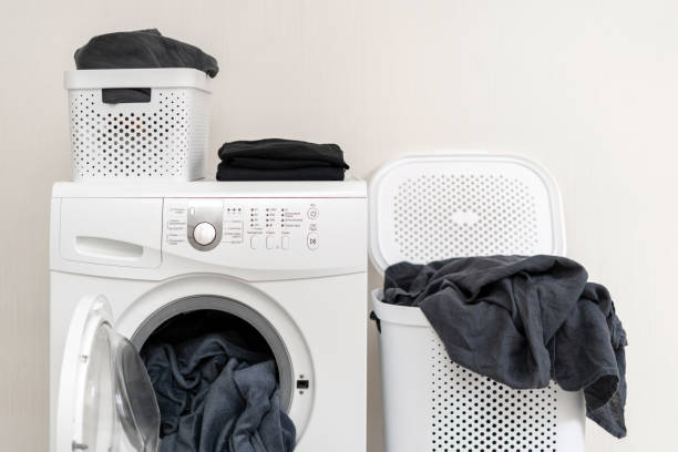 White washing machine with blanket in drum and blankets of laundry around it