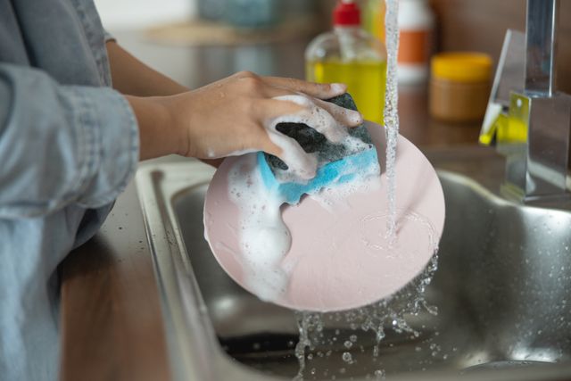 Front view of a woman hand-washing dishes in her sink.