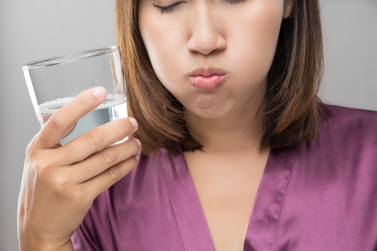 young woman winces as she tastes water from a glass