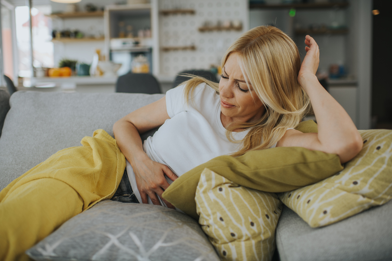 woman clutches her aching stomach on living room couch