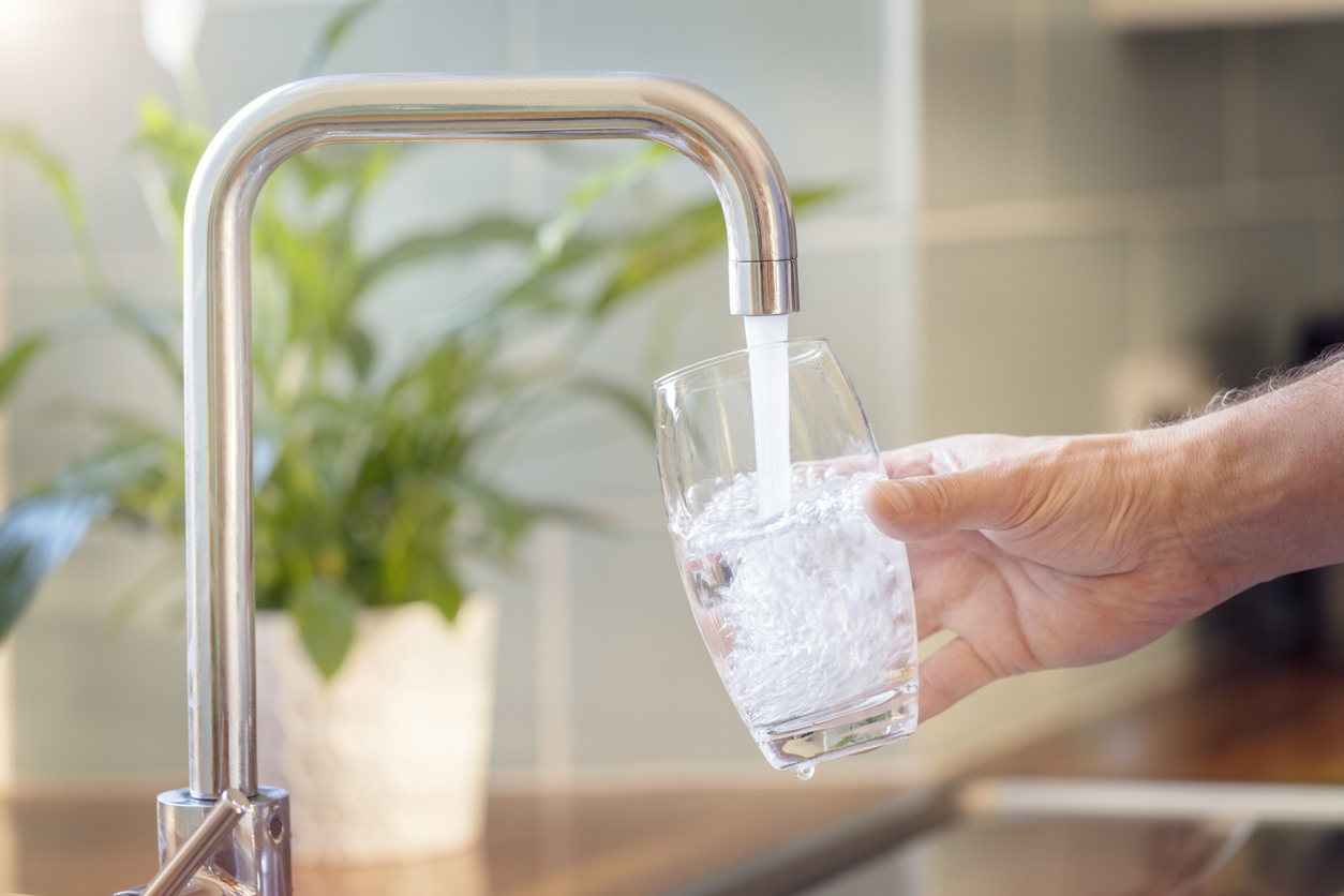 closeup of man’s hand using faucet to fill glass with water