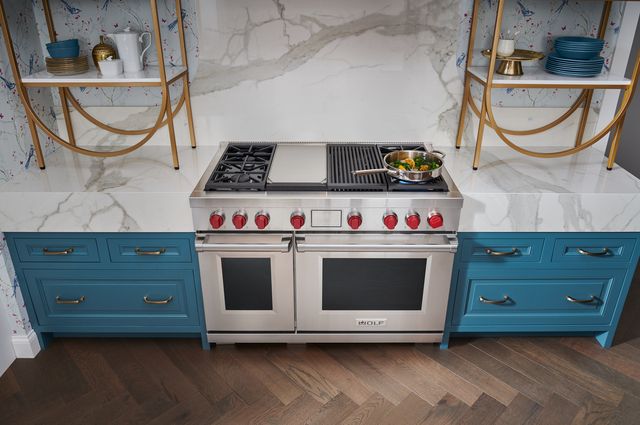 front top view of a wolf dual fuel range in a modern kitchen with a marble backsplash and countertops, and blue cabinets