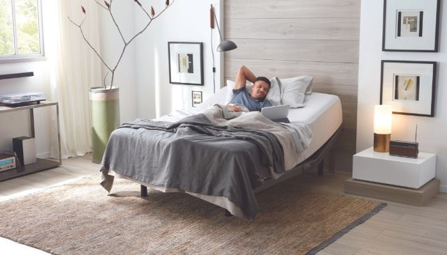 view of a modern bedroom with an adjustable bed and mattres, and a man laying on top watching his laptop