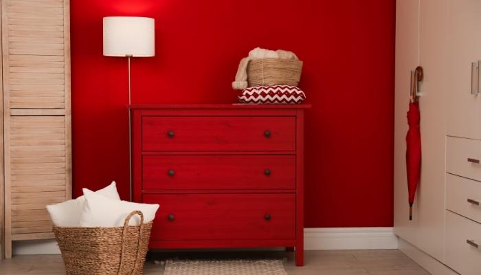 red 3 drawer dresser against matching red wall with lamp and wicker laundry basket