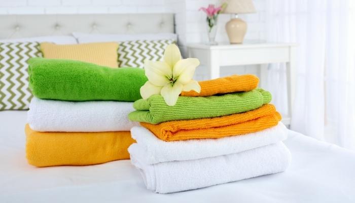 orange, white, and lime green towels folded on bed with white lily on top
