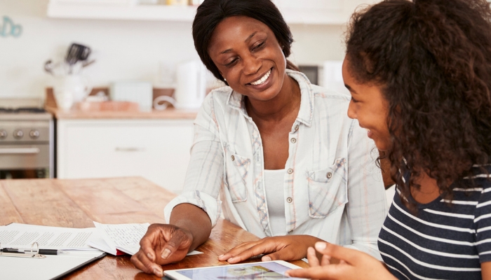 Mother helping teen with homework on digital tablet