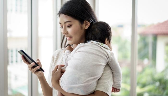 mother holding baby while using smart phone