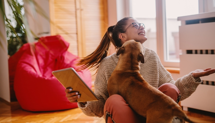 Young woman playing with her puppy and a tablet in hand