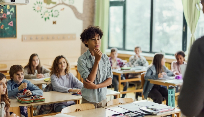 A student talking with the teacher in a filled classroom
