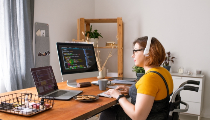 A woman in a wheelchair is happily working and concentrating on code in her home office full of natura light