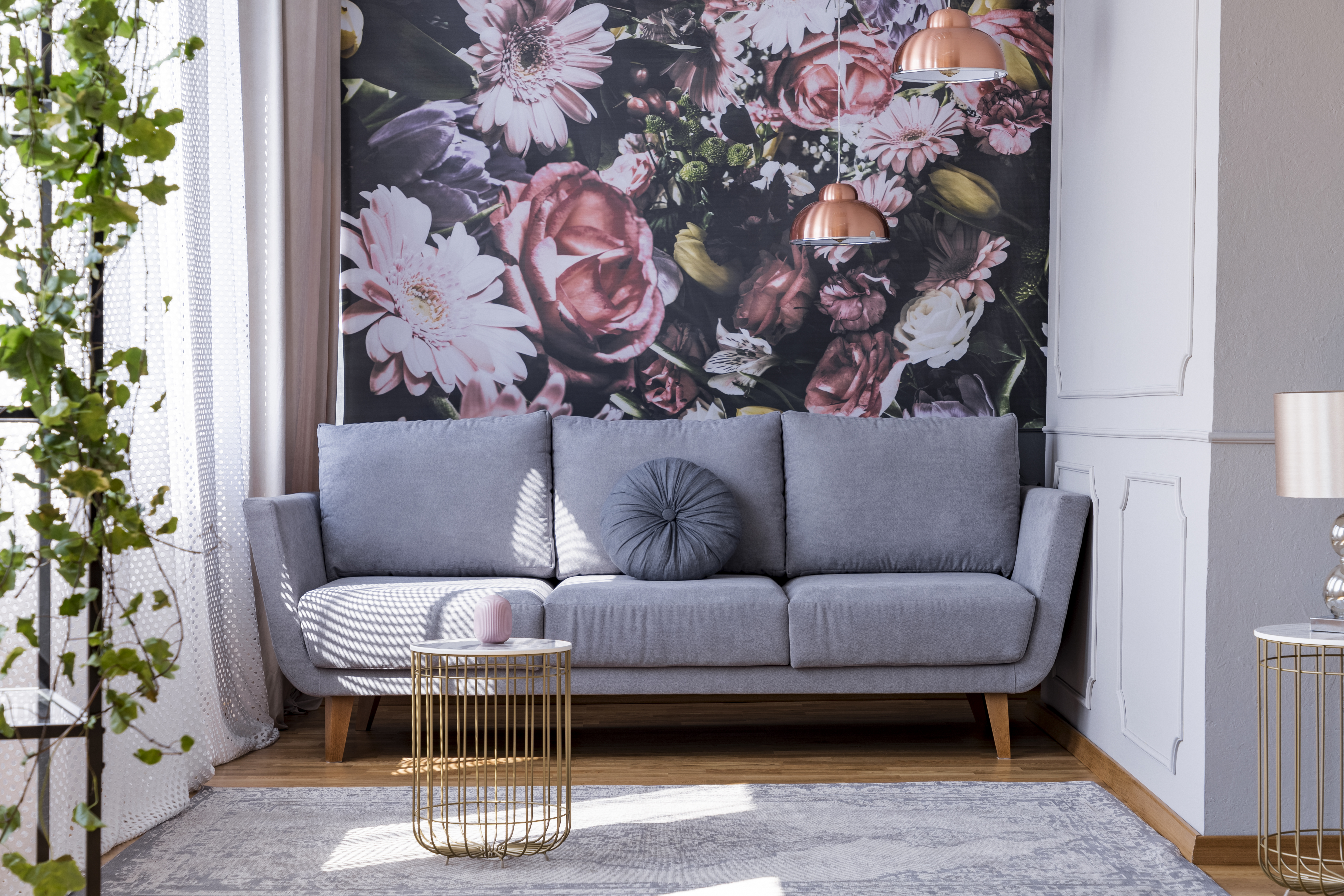 Gray midcentury sofa stated in front of floral wallpaper