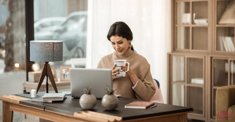 Woman holding a coffee cup working on a laptop on a desk