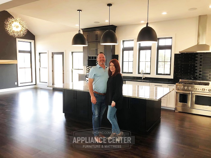 Couple standing and holding each other in front of a wide kitchen.