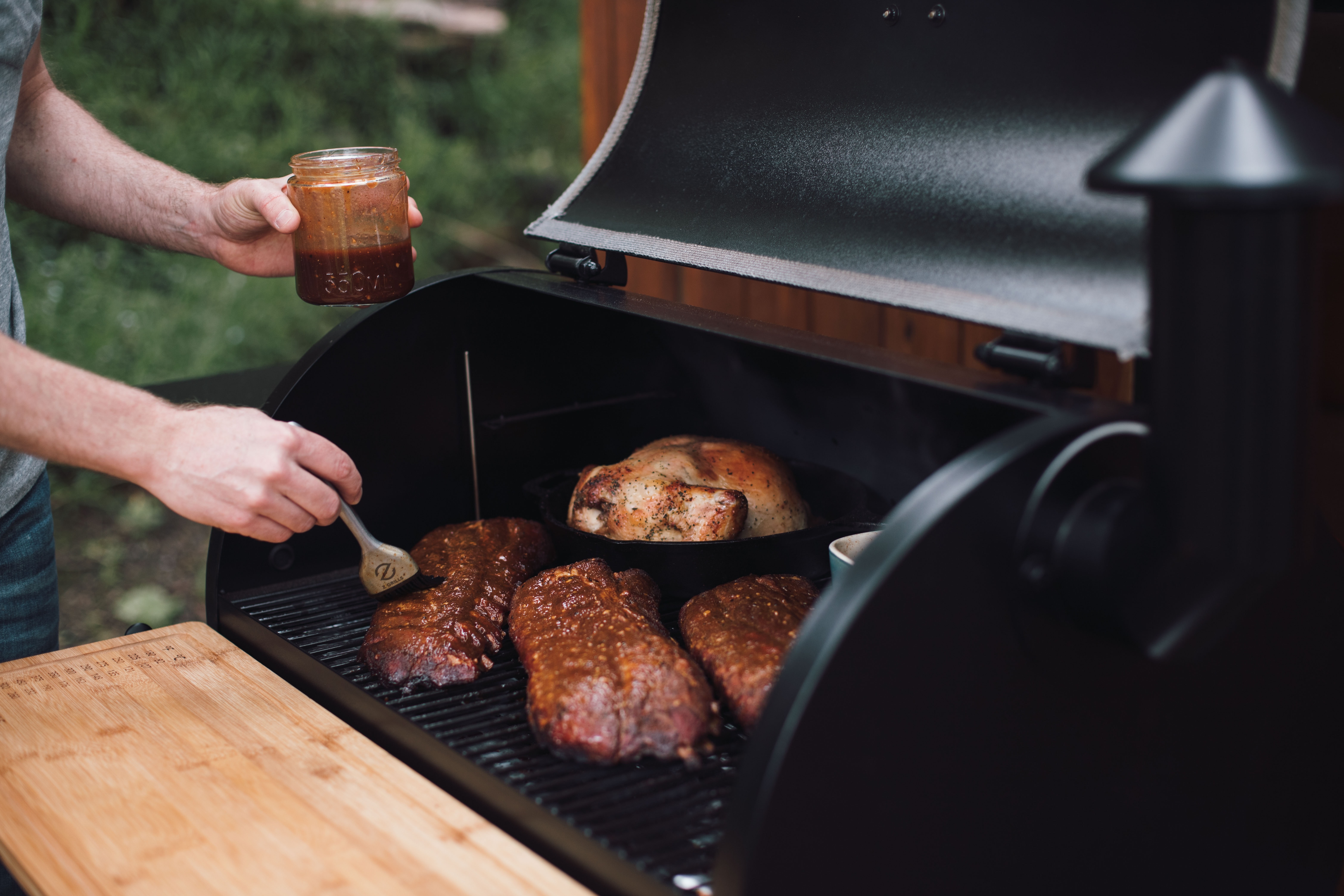 Man applying sauce to meat cooking on a grill