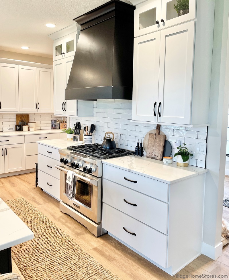 Kitchen with white painted cabinets and black painted wood range hood above a large commercial style stainless steel KitchenAid range. 