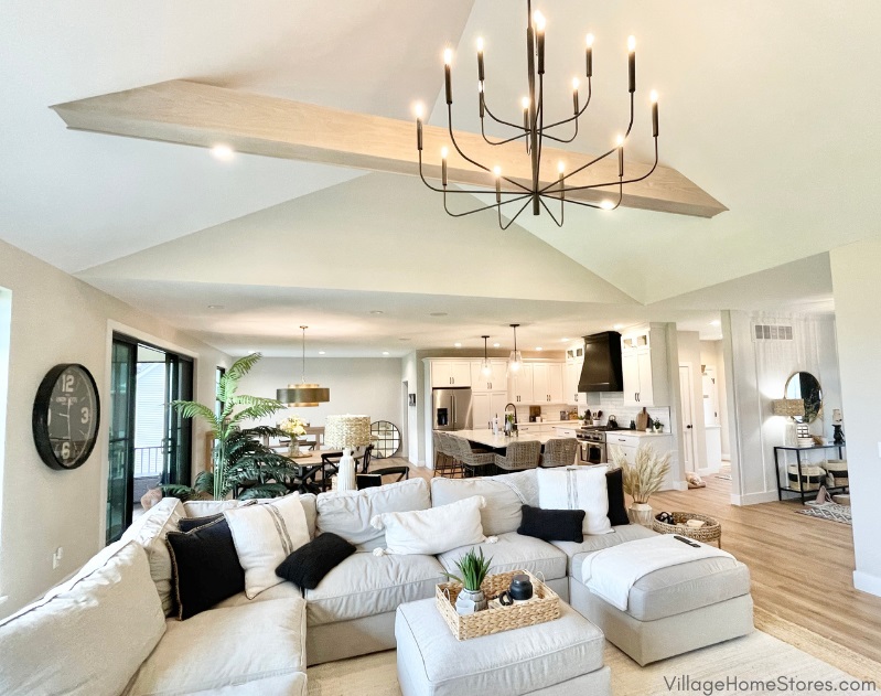 Image of great room with living room and kitchen shown. White Oak beamed ceiling and matte black chandelier in the foreground. 