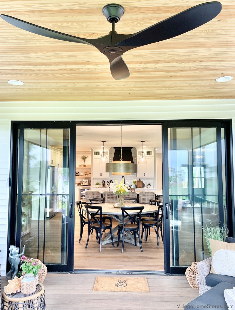 covered deck with black ceiling fan looking into great room dining and kitchen space