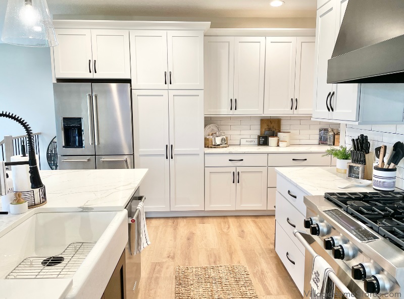 image of kitchen with white painted cabinetry, stainless steel appliances and black kitchen island and range hood. Source Credit: Village Home Stores