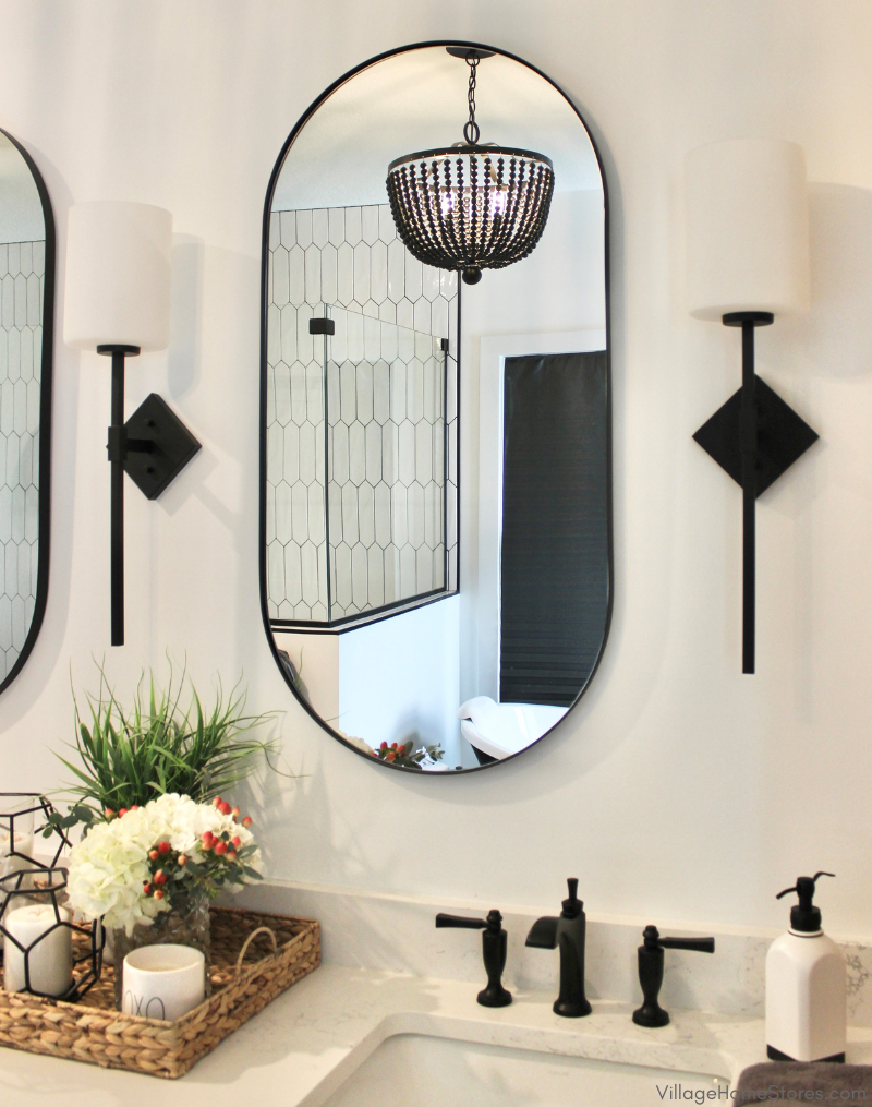Primary bathroom mirror with black wall sconces on each side and reflection of black beaded chandelier. 