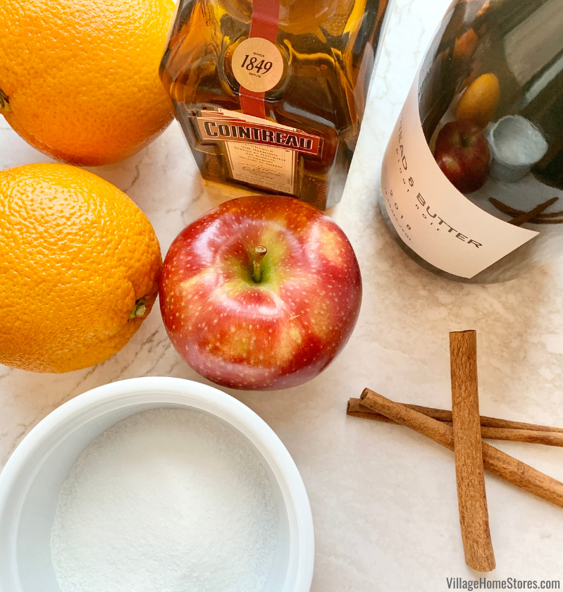 close up of Cointreau bottle, red apple, oranges, cinnamon sticks, and sugar