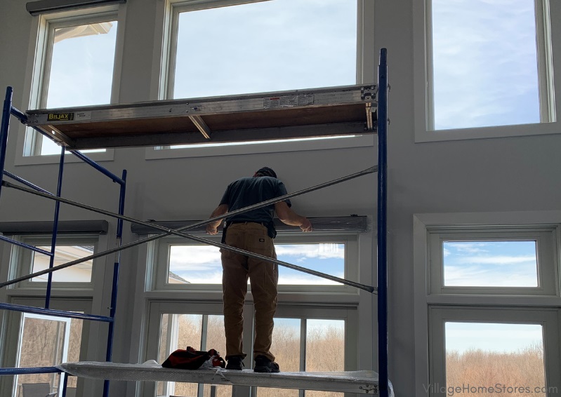 window treatment installer on scaffolding in great room
