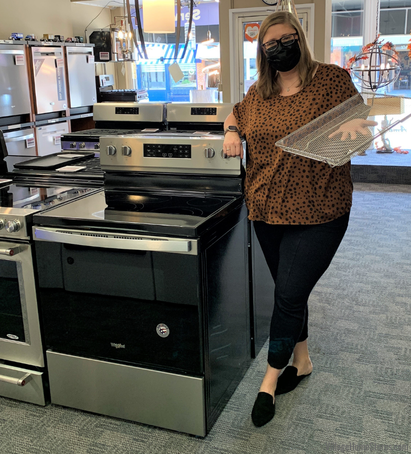Female salesperson in black facemask standing by stainless steel air fry range holding basket