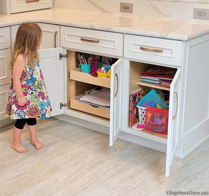Little girl in floral dress looking at open cabinet doors showing her craft supplies and coloring books in the new kitchen.