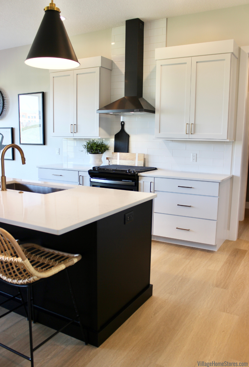 Image of white cabinet kitchen with black island and pendant lights. Black stainless chimney style range hood featured. 