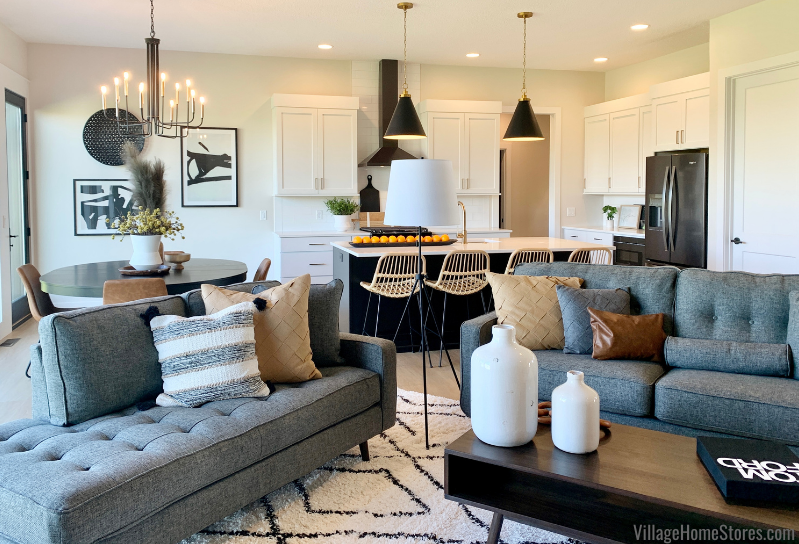 Great room open concept kitchen and living room with gray sofas and black, white and gold colors. Kitchen in background with living room in foreground. 