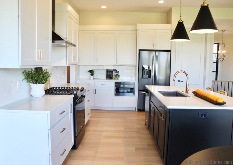 Image of kitchen with white painted cabinets, black painted kitchen island, and black stainless steel appliances. Matte black cone pendant lights hang above the kitchen island. 