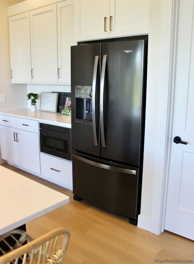 Image of black stainless steel French door refrigerator installed in a white cabinet kitchen. Koch cabinetry and Whirlpool appliances for this Bettendorf home by Village Home Stores.