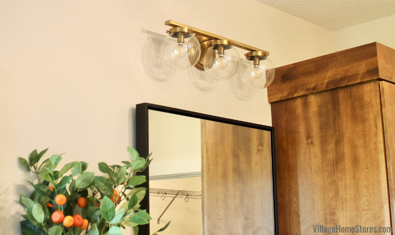 Close up shot of brass and round glass 3 light vanity fixture by Savoy House from Village Home Stores.