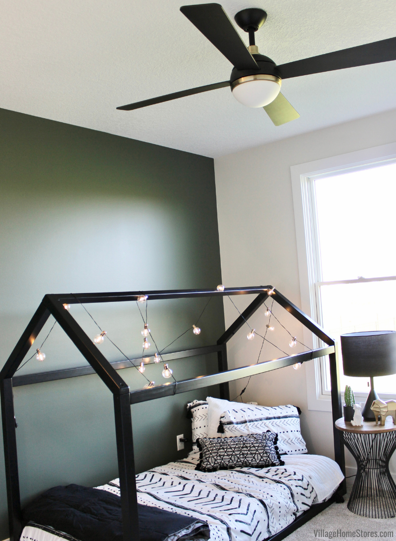 Image of children’s room with black house frame post bed with wrapped fairy lights and modern black ceiling fan.