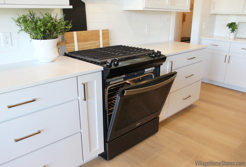 Whirlpool black stainless gas range with full width grates and oven door slightly ajar.