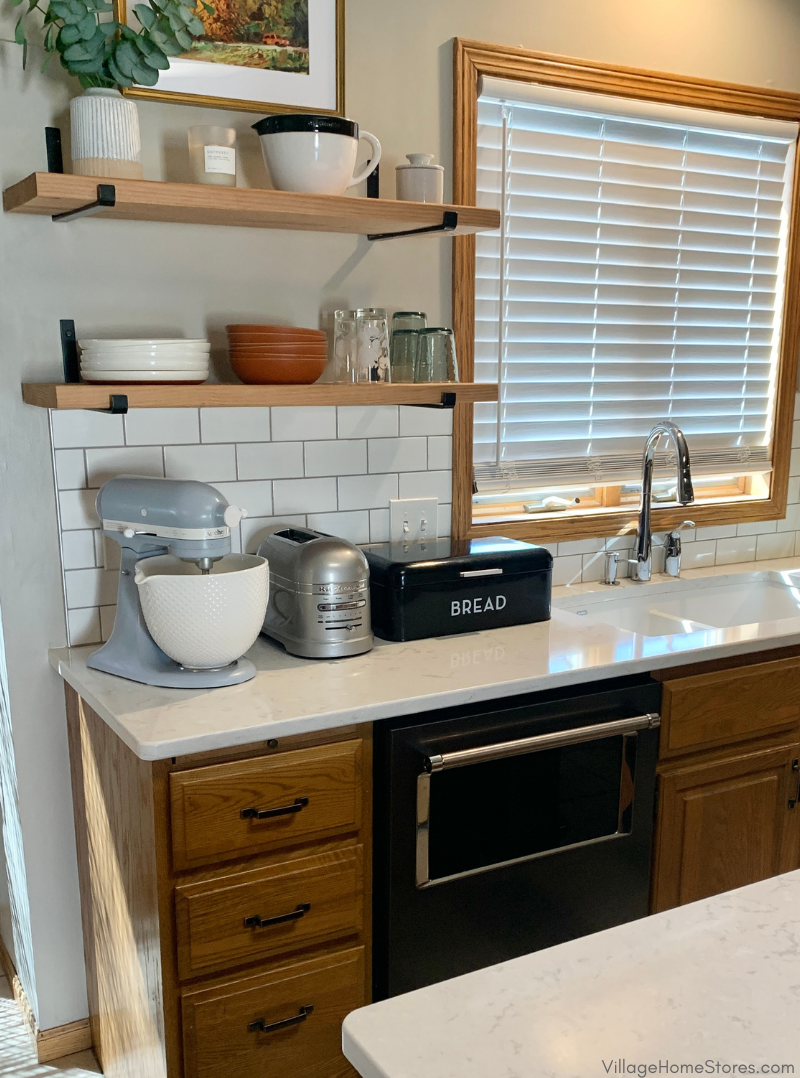 Open shelf in oak kitchen with black metal brackets and white subway tile on wall