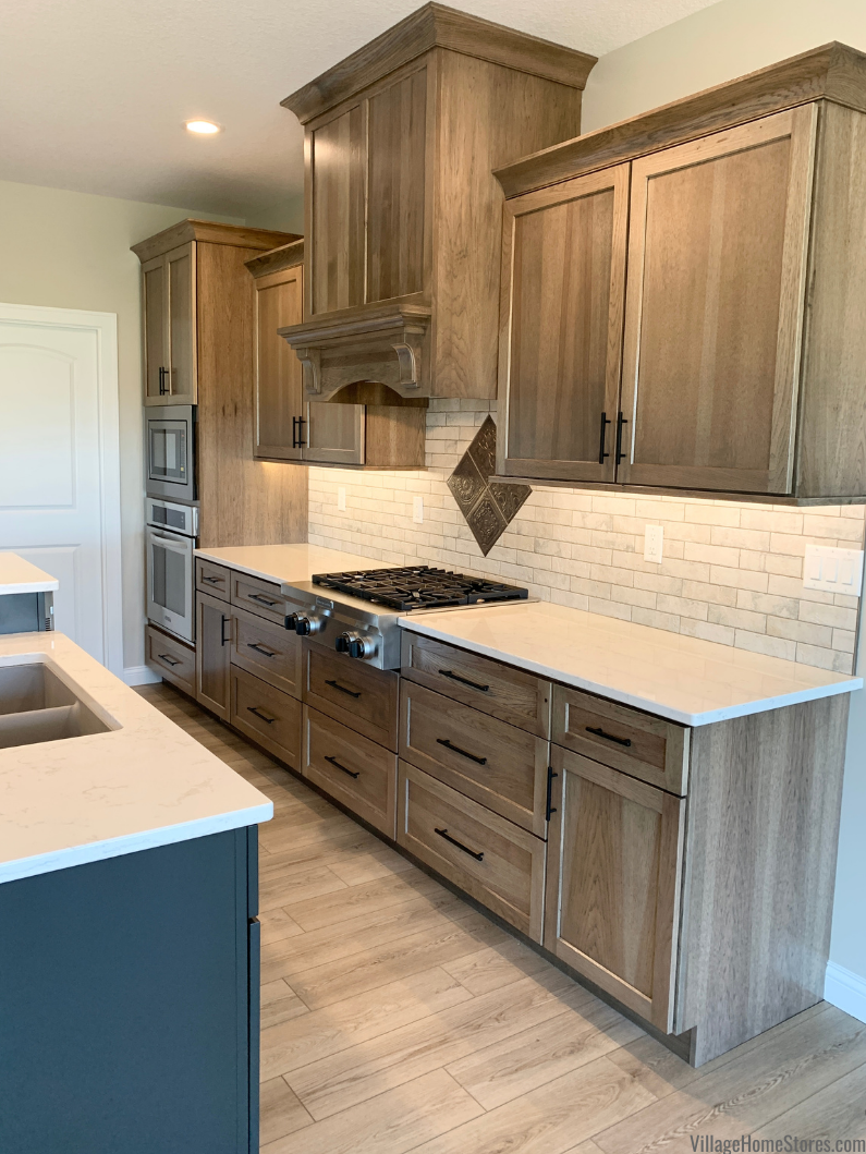 Kitchen cabinets with wood hood and cooktop below. Hickory cabinetry in Morel stain from Dura Supreme Cabinetry Village Home Stores. 
