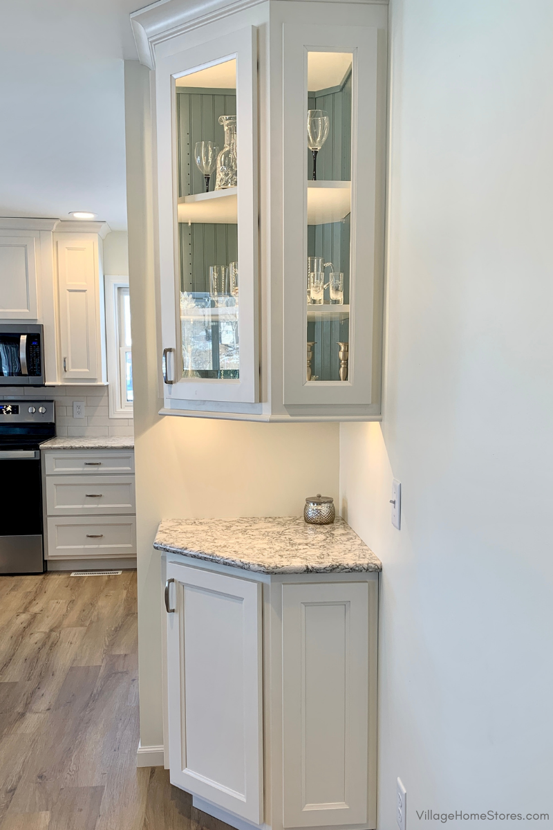 angled end cabinets in kitchen with upper cabinet prepped for glass doors and an accent beadboard paneled back