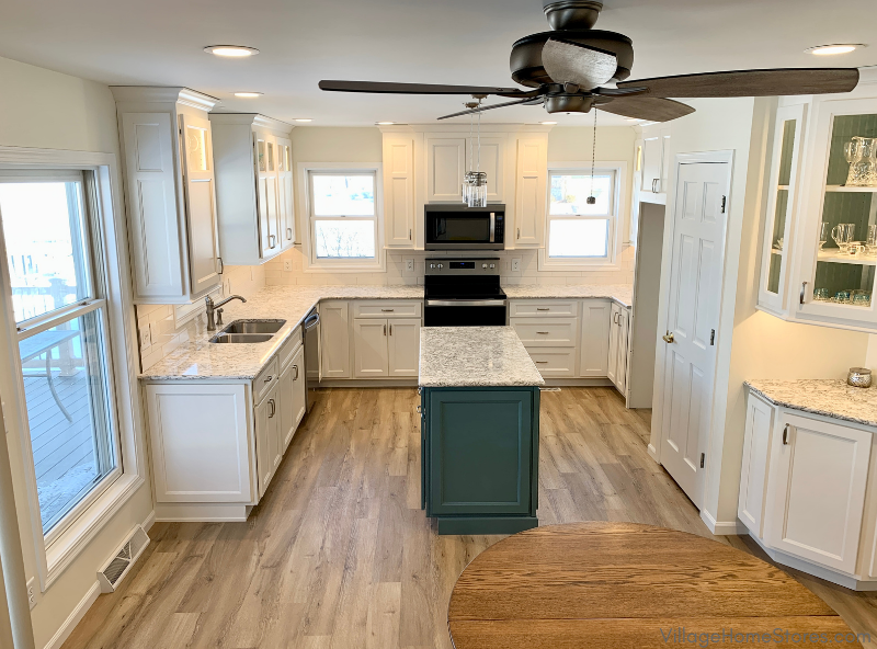 Image of lake house kitchen with U shape layout, small teal kitchen island, and ceiling fan in foreground 