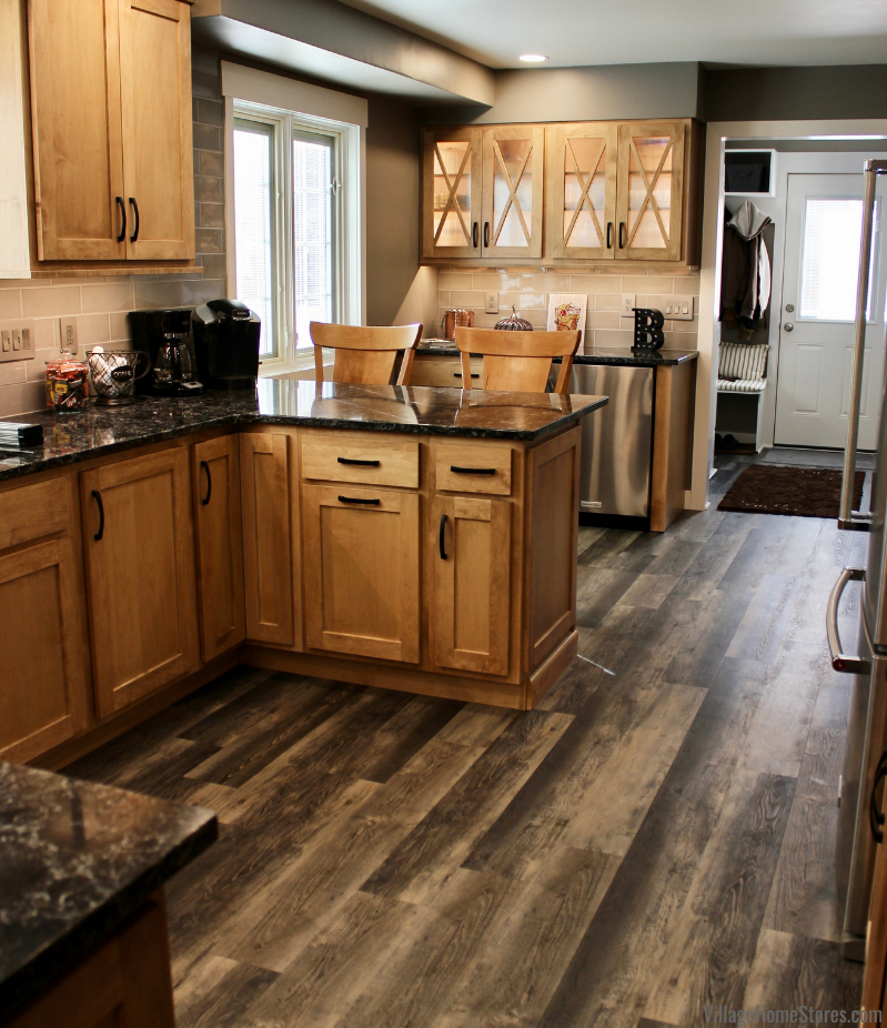 Image of kitchen peninsula and glass door cabinets behind it. Maple Pecan stained cabinets and dark quartz counters featured