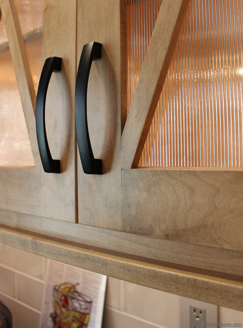 Close-up shot of Maple Pecan stained cabinet doors with x-mullions and reeded glass inserts. Black handle hardware also featured