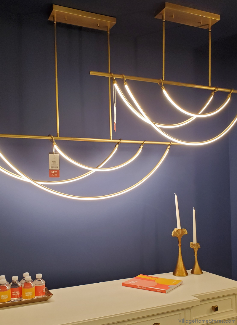 draping LED light chandelier with brass metal hanging above white dresser with blue painted wall behind