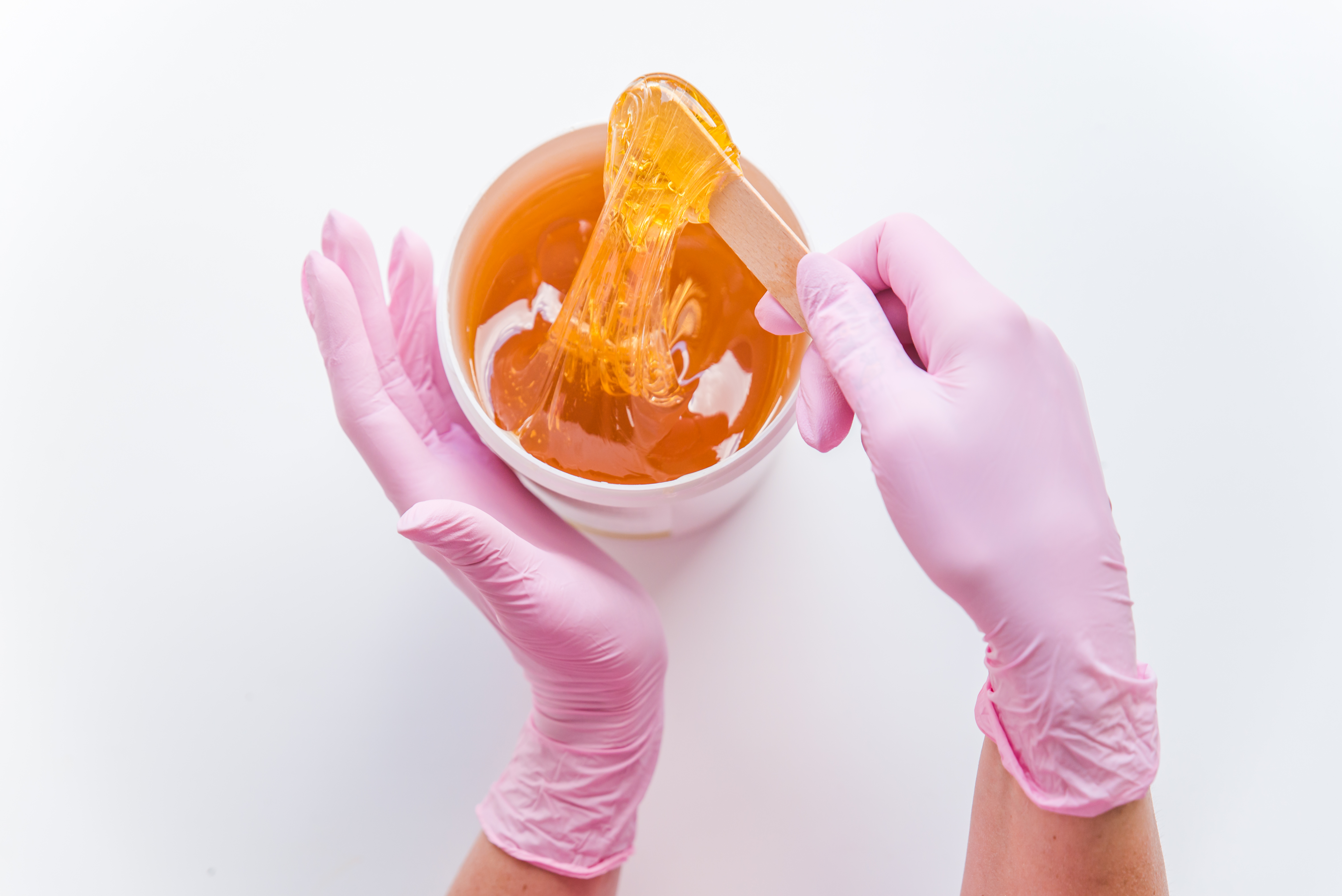 Person in pink gloves performs sugaring process with honey