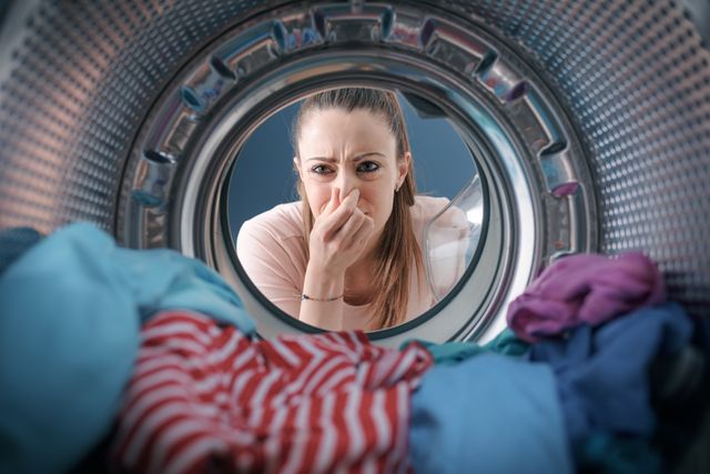 view from the inside of washing machine of a woman holding her nose in front of wet clothes in the washer