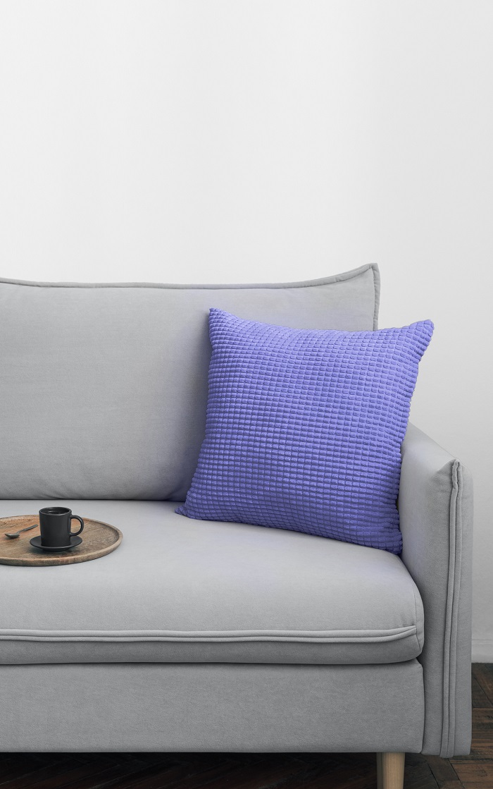 Periwinkle pillow sitting on a gray couch. 