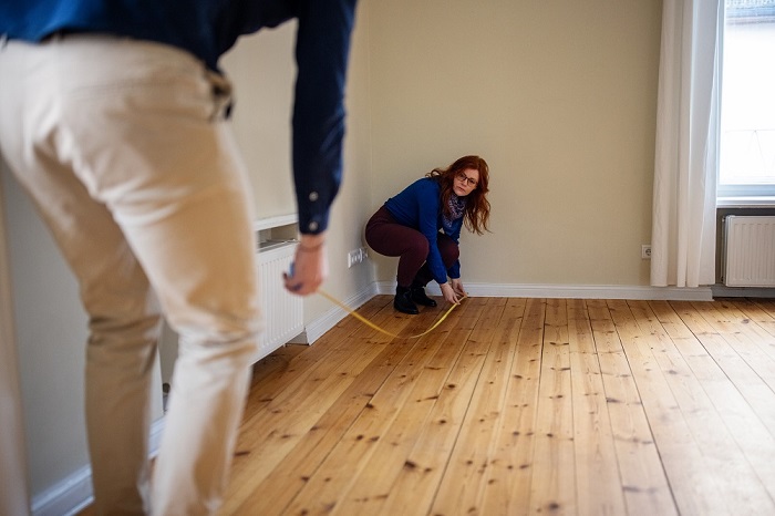 Woman measuring hardwood floor with a tape measurer. 