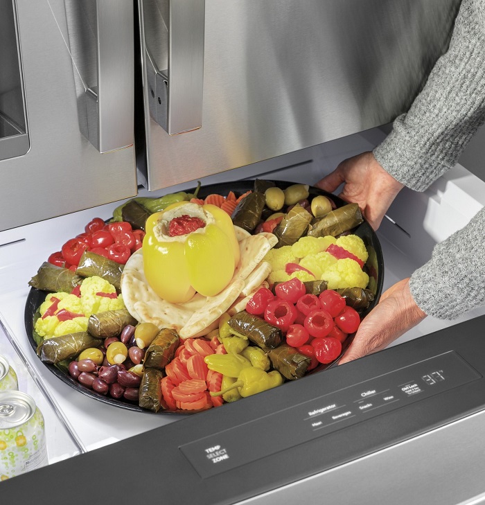 Set of hands placing a deli tray into a food drawer of the fridge.