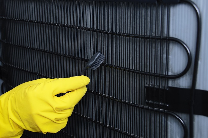 A rubber gloved hand using a brush to clean bottom plate of fridge.