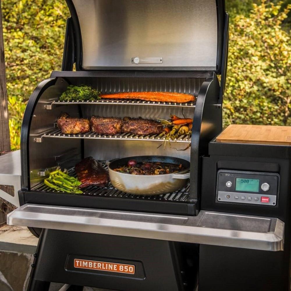 Traeger grill with lid open showing off meats, vegetables, and a pan on the bottom rack.